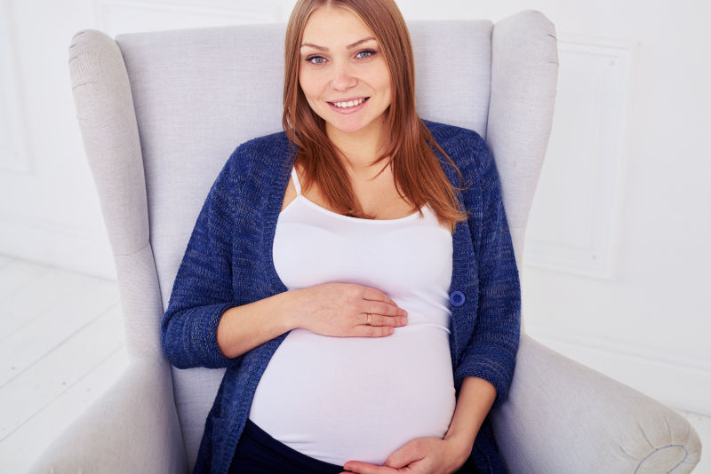 坐在沙发上用手托着肚子的孕妇