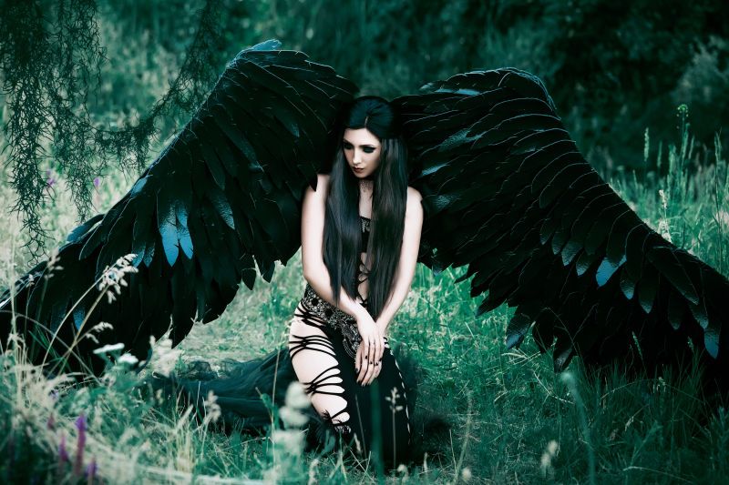 拥有黑色翅膀的美女恶魔跪在森林中