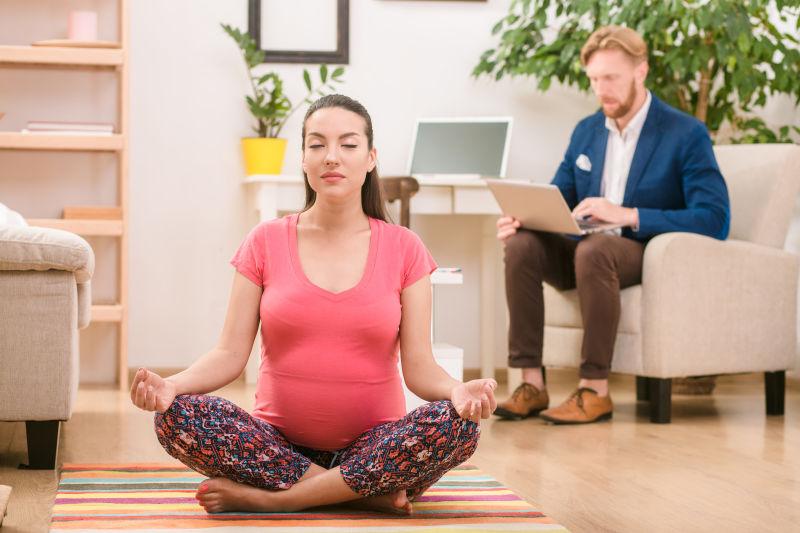 做瑜伽的孕妇和在沙发上用笔记本电脑工作的丈夫