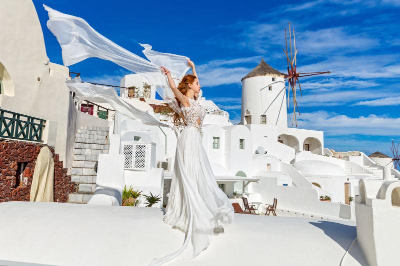 圣托里尼建筑背景下穿白色礼服的女子