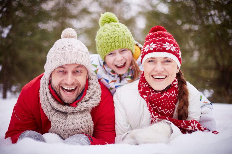 森林背景下冬日里趴在雪地上微笑的一家人