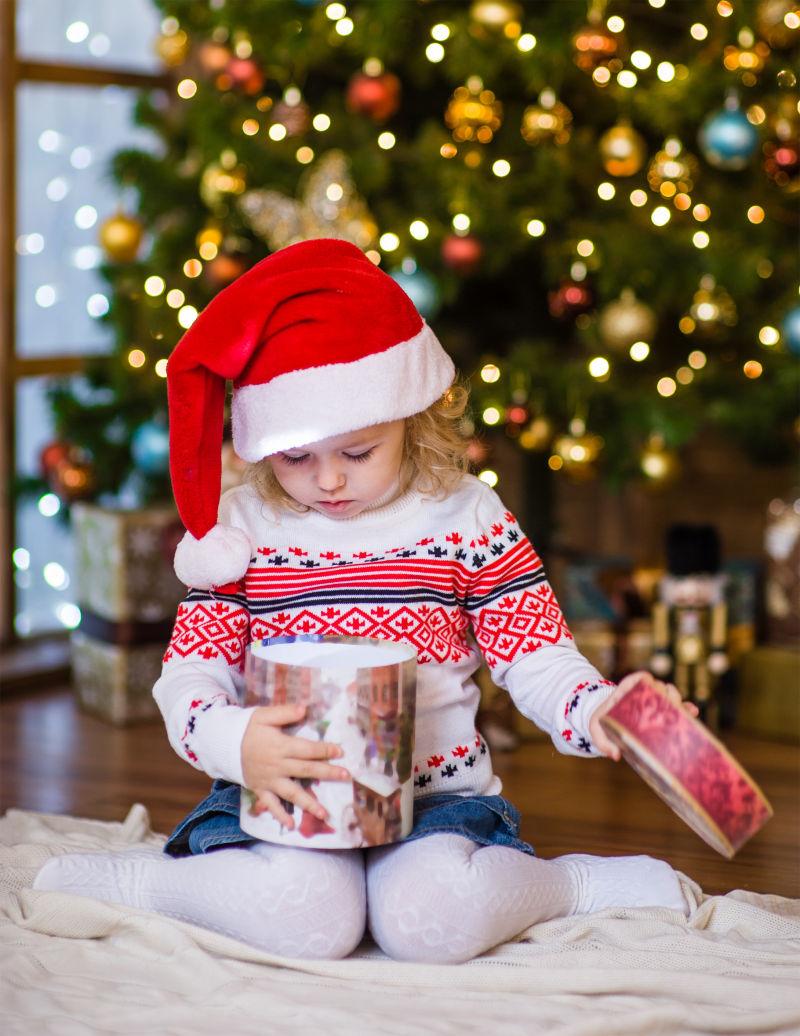 戴着红色圣诞帽子看向礼物盒的可爱宝宝