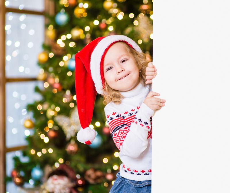 小女孩戴红色圣诞老人帽子后面白板上