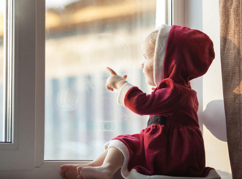 穿着圣诞衣服的小女孩看着窗外