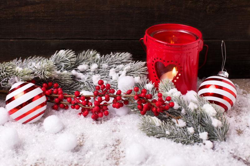 雪地上的红色蜡烛和圣诞树枝和浆果和圣诞铃铛