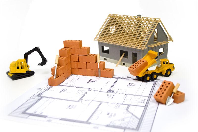 白色背景下的图纸上的工程建设砖工程车和房屋模型