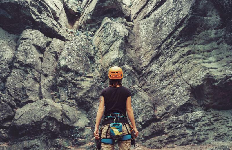 身穿攀岩设备的年轻女子站在山脚下