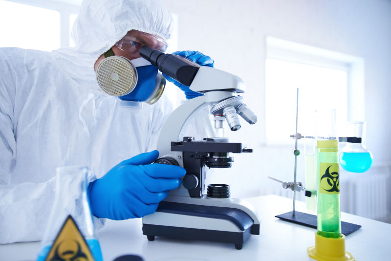 穿着防护服的男性科学家在显微镜下研究新的化学物质