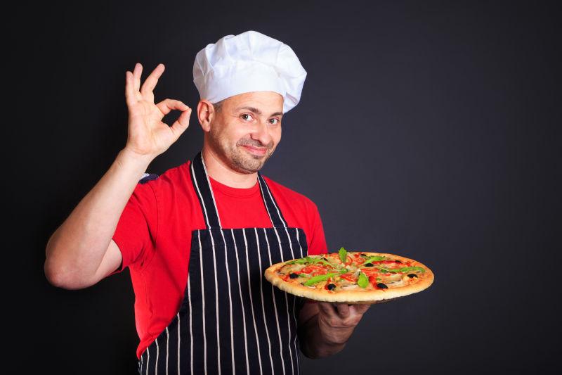 拿披萨的迷人的厨师做出ok的手势