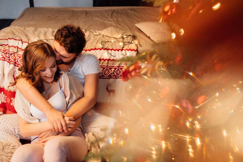 情侣们穿着睡衣躺在靠近圣诞树的床上的地板上