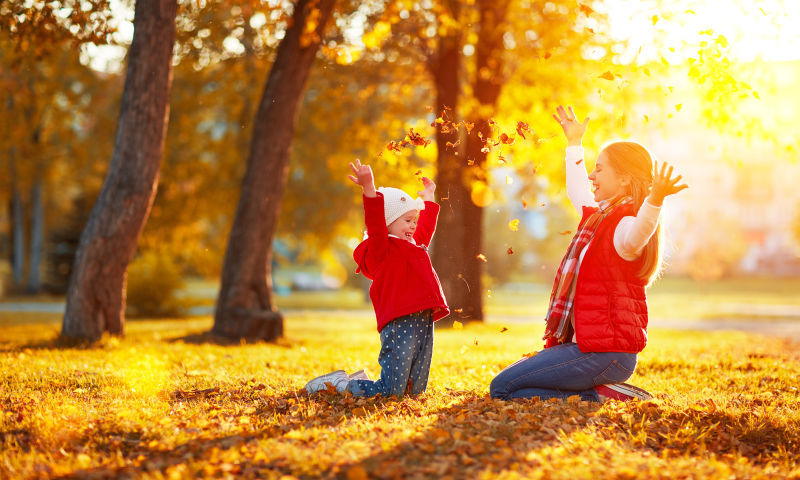 母亲带着孩子在秋季公园玩耍扔树叶