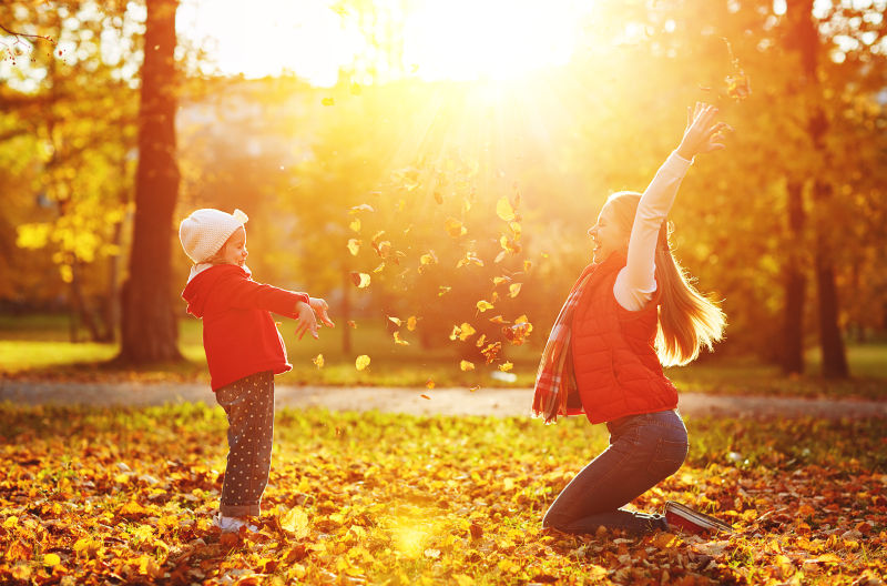 母亲和孩子在秋季公园玩耍扔树叶
