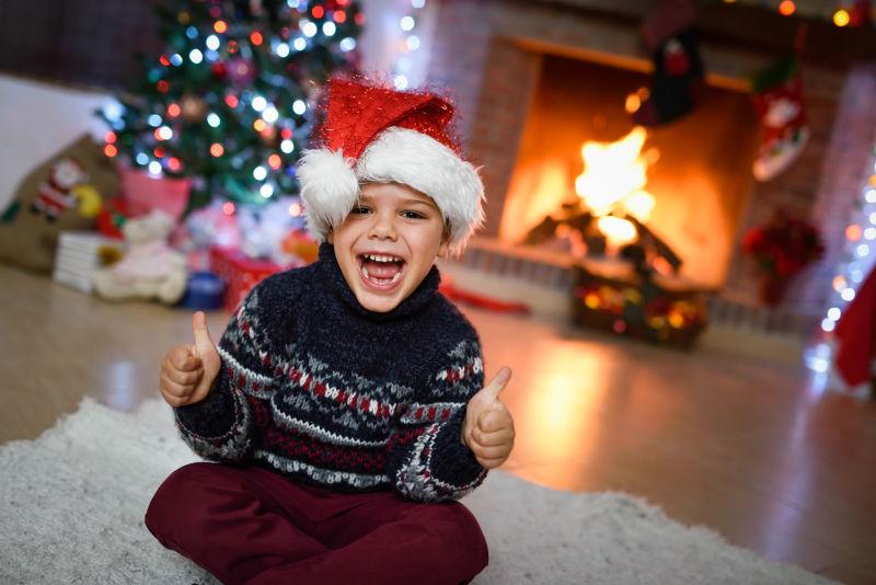 房间里戴着圣诞帽坐在地上竖起大拇指的小男孩