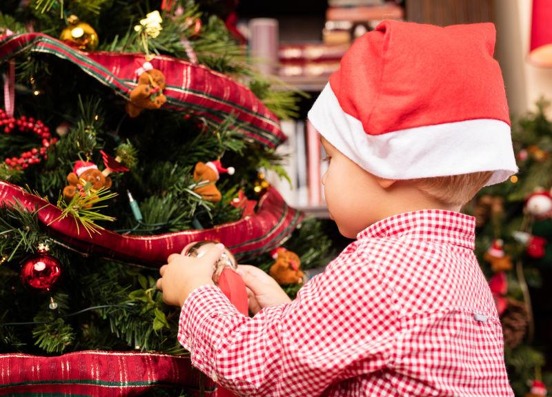 戴着圣诞帽的小孩正在装饰圣诞树