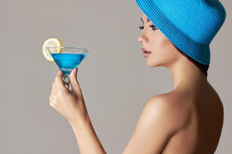 带着蓝色帽子的美女端着一杯蓝色鸡尾酒