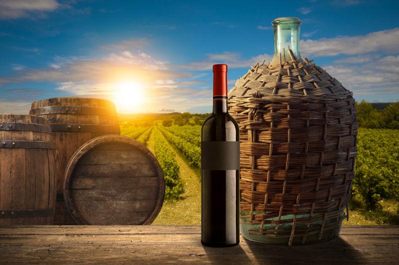 有阳光的葡萄园背景下的酒桶和一瓶红酒
