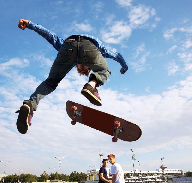 蓝天白云城市里玩滑板跳跃的年轻人