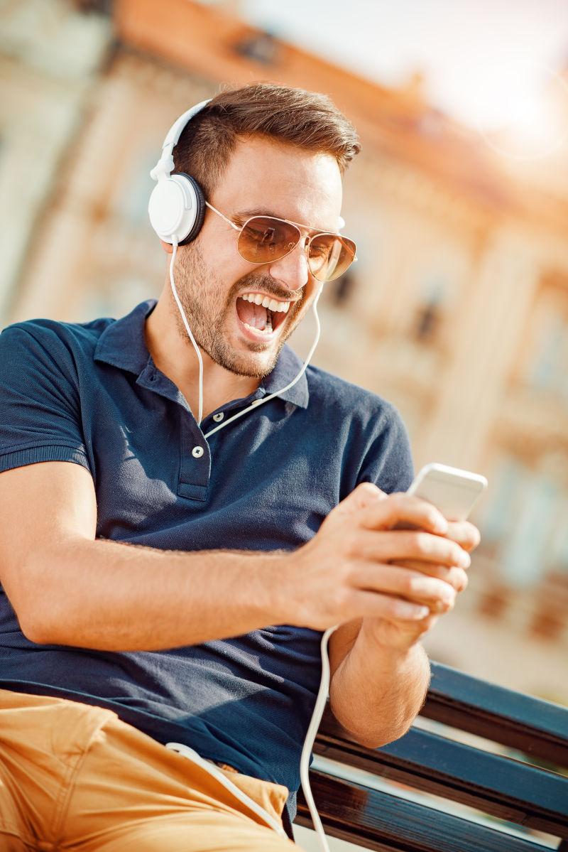 坐在户外长椅上玩手机听音乐的男人