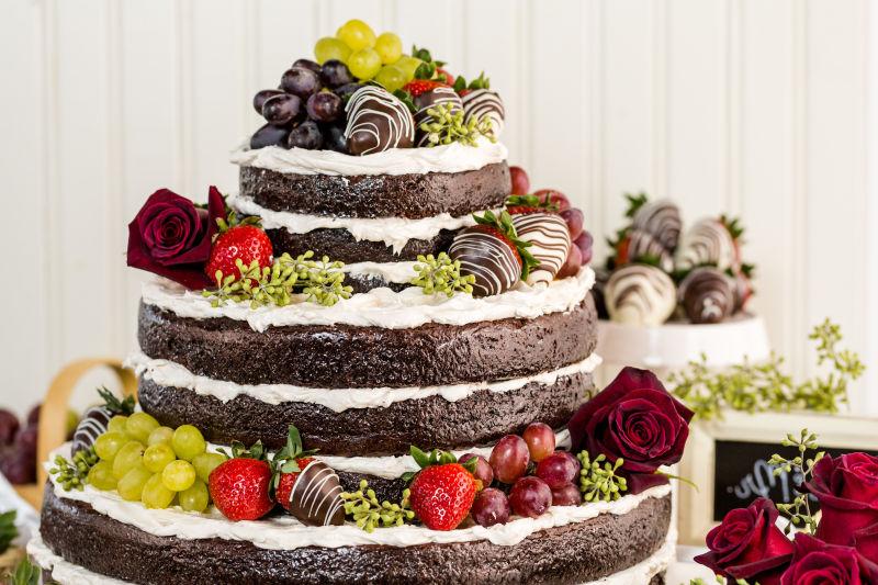 白色背景上的带有玫瑰花和水果的巧克力婚礼蛋糕