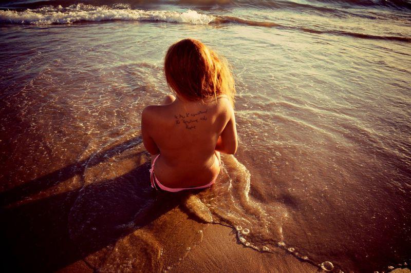 阳光下坐在沙滩上背部有纹身的美女背影