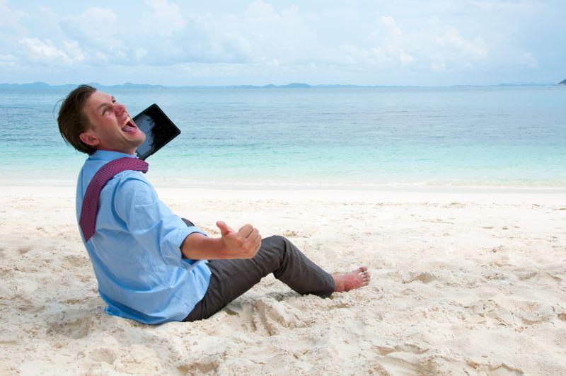 拿着平板电脑开心的坐在沙滩上的男人