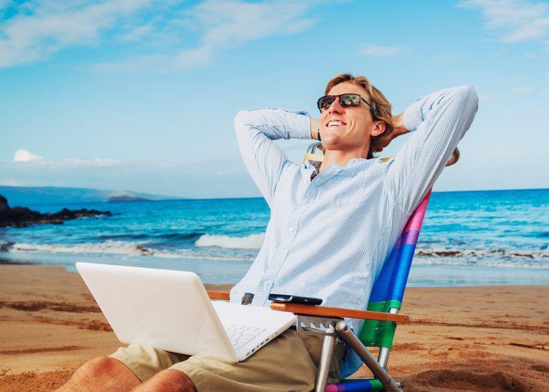 腿上放着笔记本电脑靠在沙滩椅上的男人