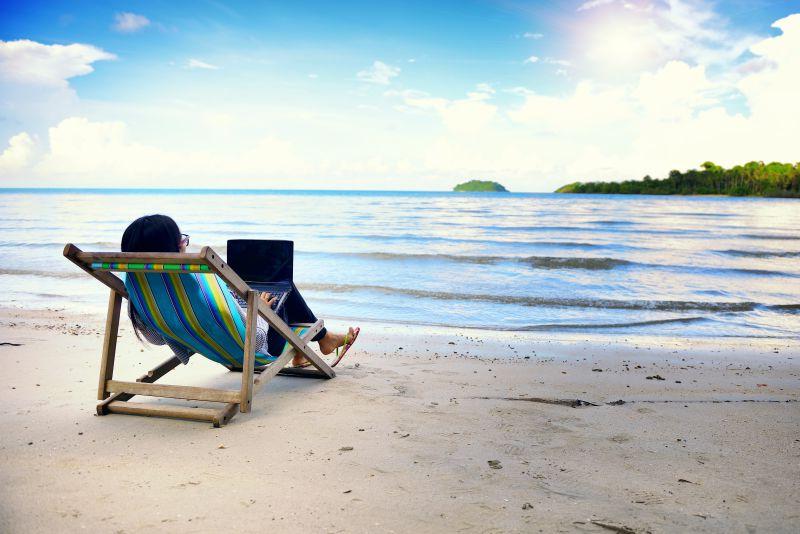 海边沙滩旁躺在躺椅上使用笔记本电脑的女人