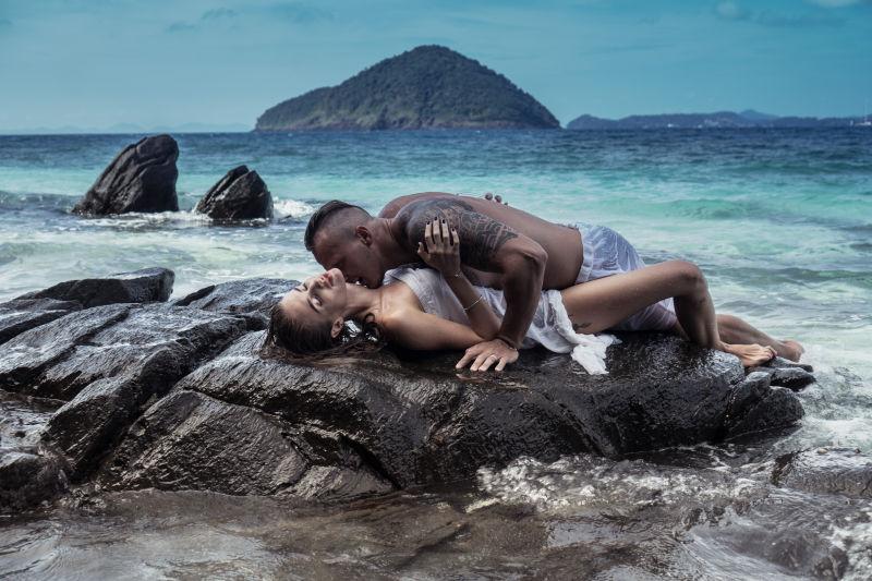 性感的年轻情侣在海边岩石上