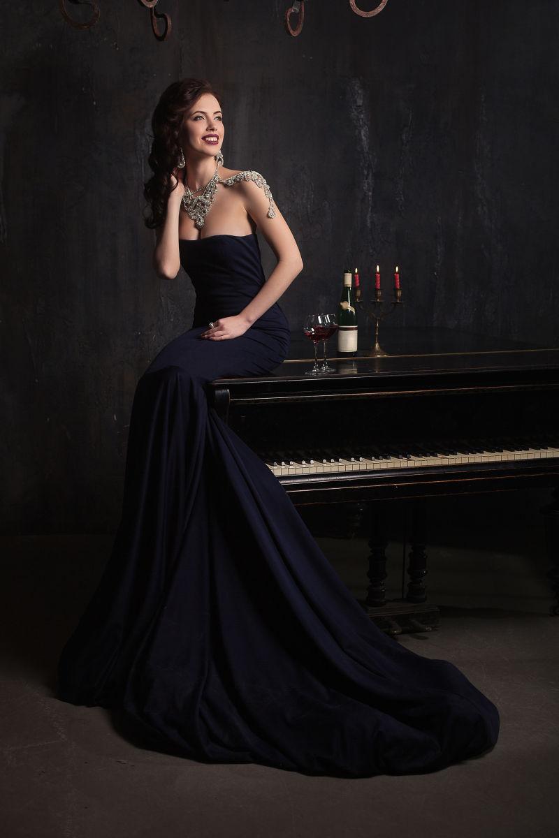 美丽的年轻女子穿着黑色的裙子坐在钢琴上