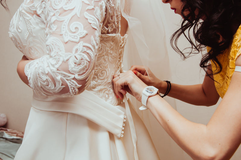 美丽的伴娘帮助新娘在婚纱上系蝴蝶结