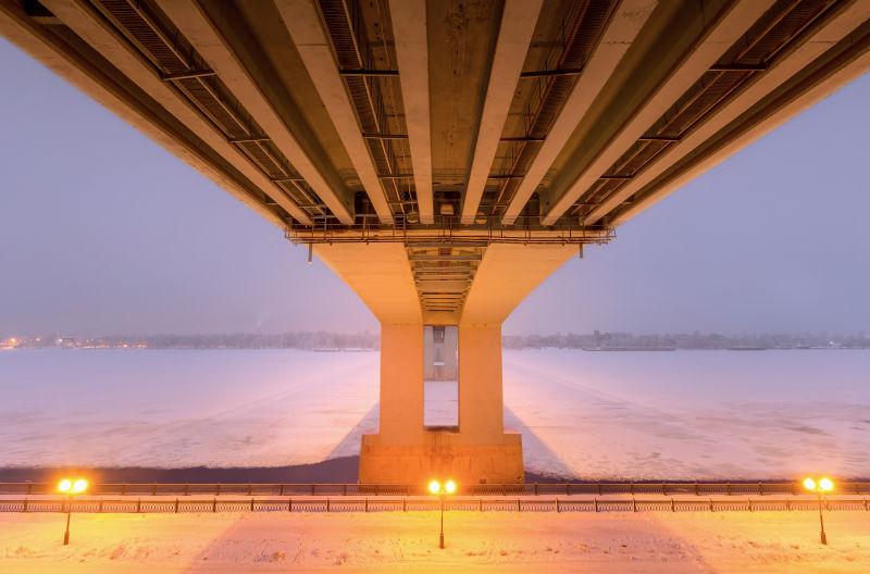 黎明-夜幕时分两者灯的冰冻河上的大桥底部