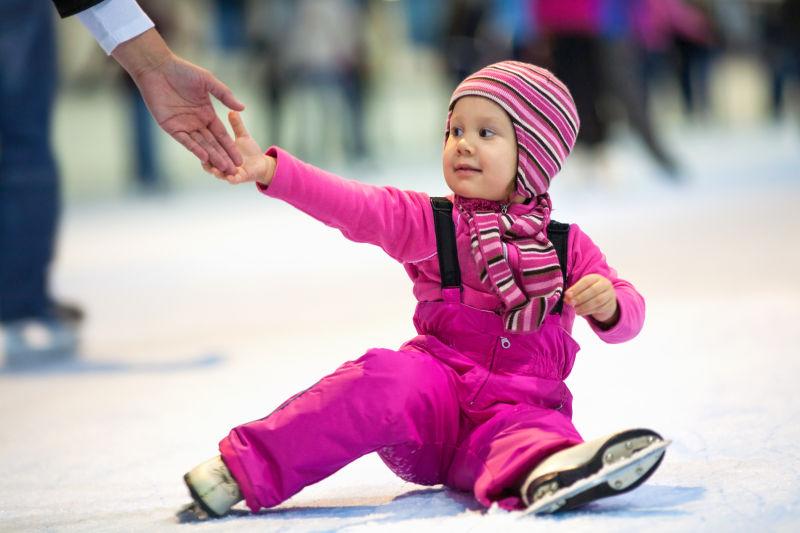 漂亮的小女孩坐在溜冰场的溜冰场上