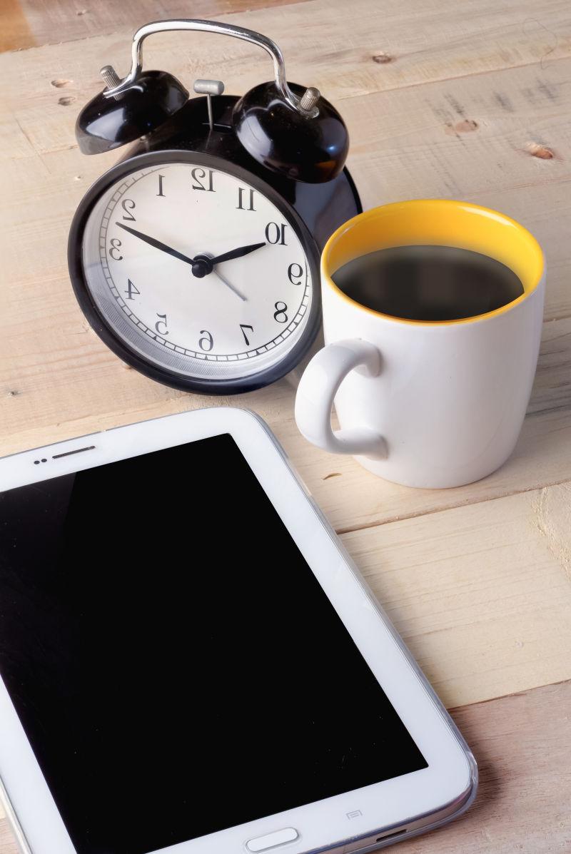 木纹理桌上的闹钟和智能手机旁边的一杯咖啡