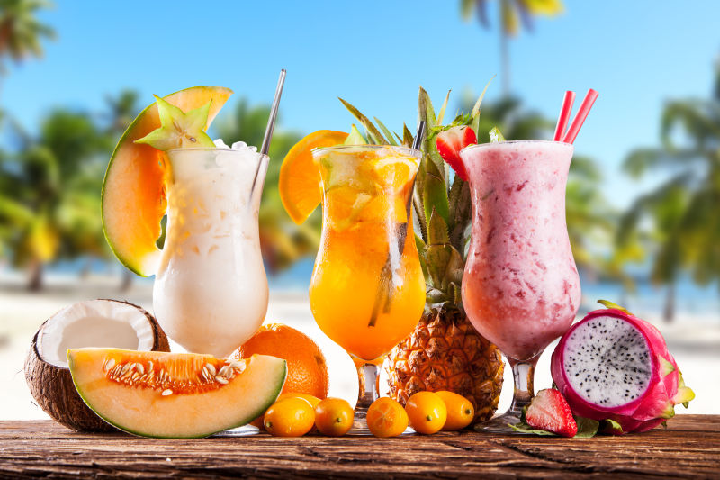 沙滩木桌上放着三杯夏日水果饮品与水果