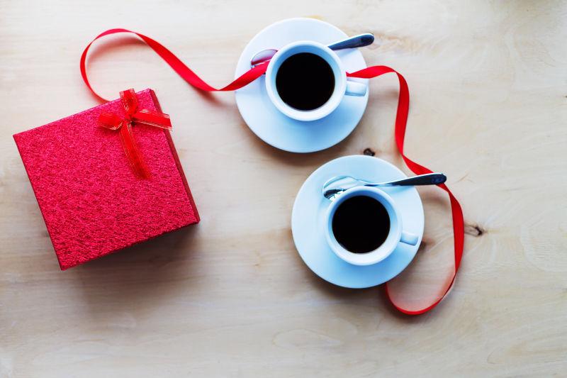 桌子上的红色礼物盒边有两个咖啡杯