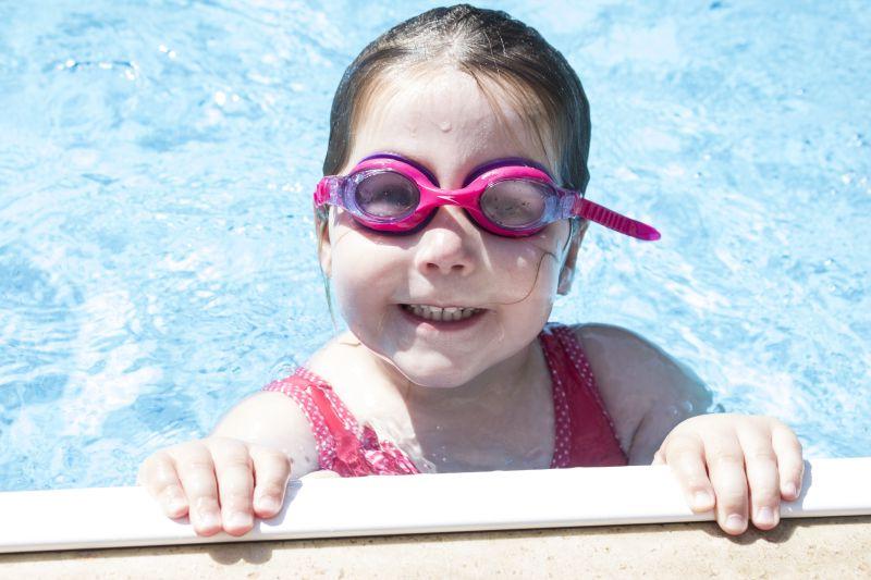 微笑的学龄前女孩在泳池里戴护目镜