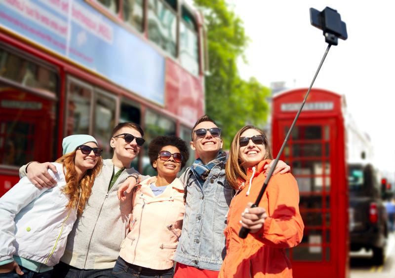 伦敦城市街道背景下带智能手机和单足的微笑青少年朋友组