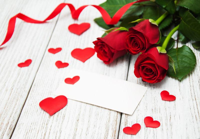 装饰着玫瑰花束和红色丝带的木板上有一张空白贺卡