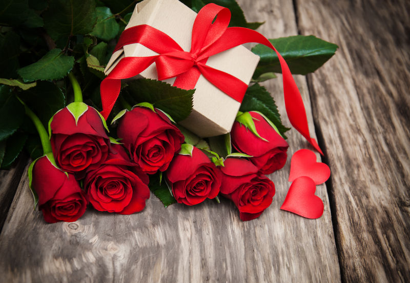 木板上美丽的红玫瑰花束上有个礼物盒