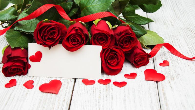 木板上玫瑰花束下放着一张空白情人节贺卡