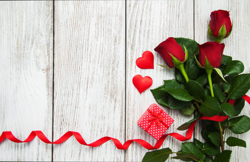 木板上的玫瑰花束和红色丝带和礼物盒