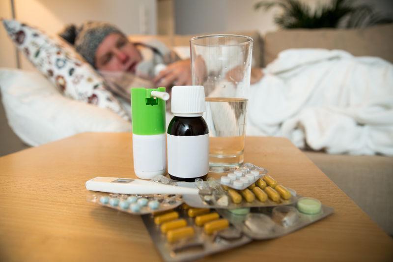 床上躺着感冒的病人桌子上摆满了各种感冒药