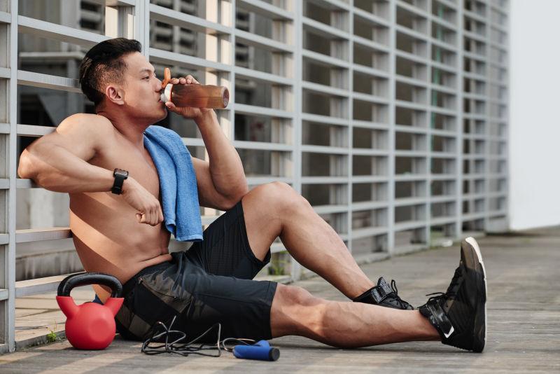靠坐在栅栏上的肌肉男喝着运动饮料 