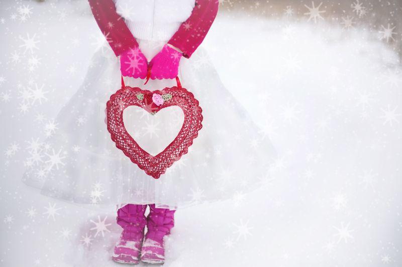 穿着白色长裙的姑娘在雪地上提着一个红色的爱心