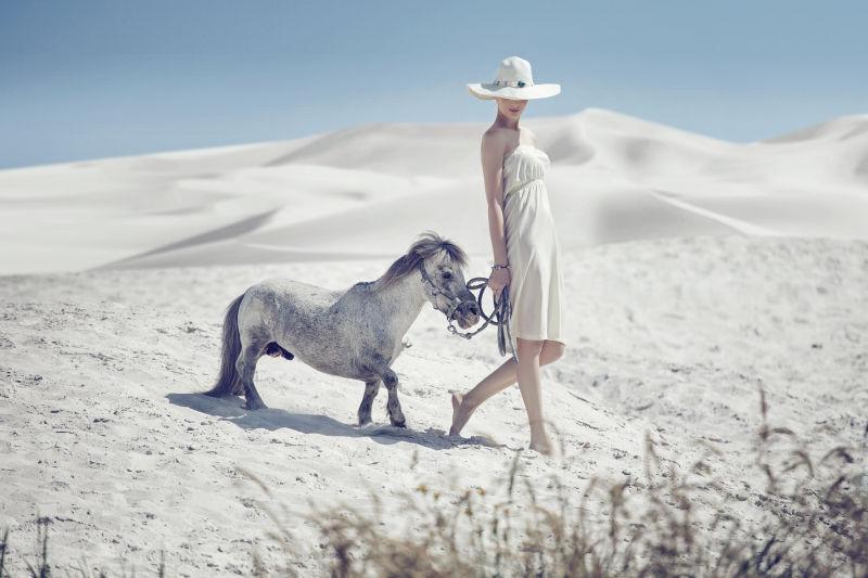 美女牵着马在沙漠中行走