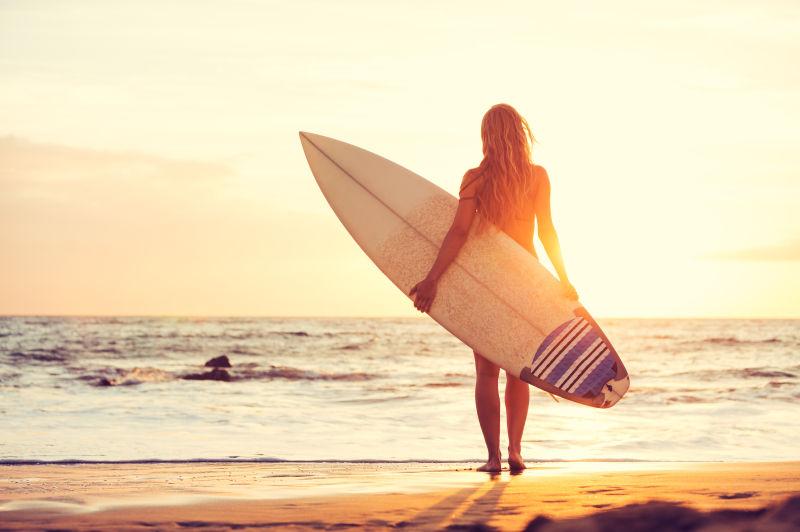 在海边手拿冲浪板的年轻女子