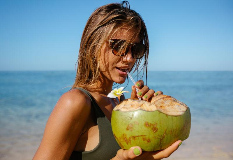 在海边喝椰子汁的年轻女子