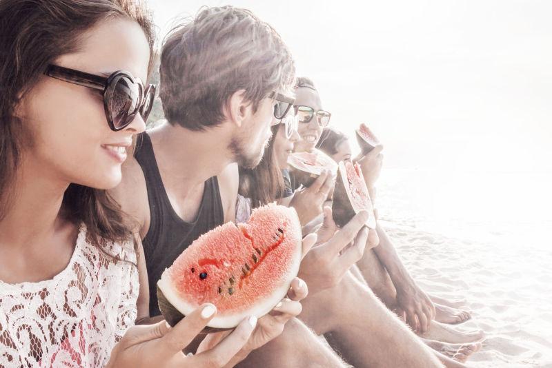 坐在海滩上吃西瓜的一群年轻人