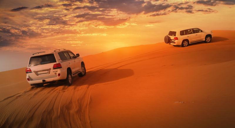 夕阳下的沙漠上的两辆越野车