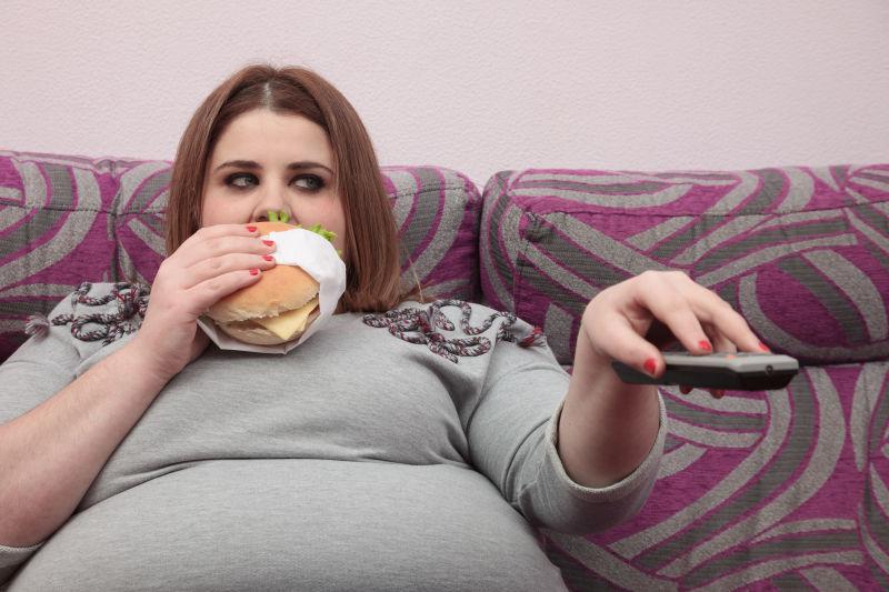 沙发上吃着汉堡拿着遥控器的肥胖女人